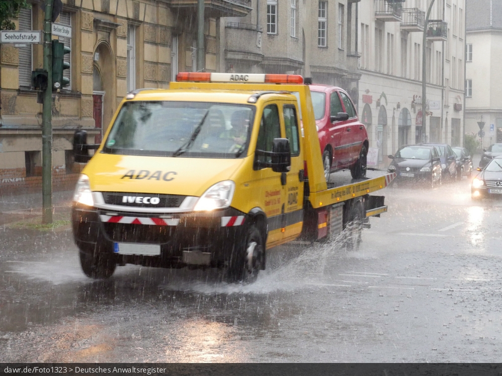 Dieses Foto zeigt einen Abschleppwagen, wie während eines starken Regens durch eine Pfütze fährt. Dieses Bild ist gut als symbolische Darstellung für die Themen Unwetter und Starkregen geeignet.