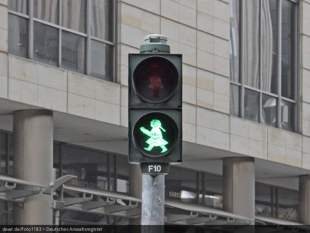 Dieses Foto zeigt eine grüne Fußgängerampel, welche die Ampelfrau (die weibliche Version des berühmten ostdeutschen Ampelmännchens) als Symbolik verwendet. Diese Darstellungsform wurde erst 1996 vom Graphiker Hans-Jürgen Ellenberger im Sinne der Geschlechtergerechtigkeit entworfen und wird allerdings nur von wenigen Städten bei Lichtsignalanlagen verwendet.