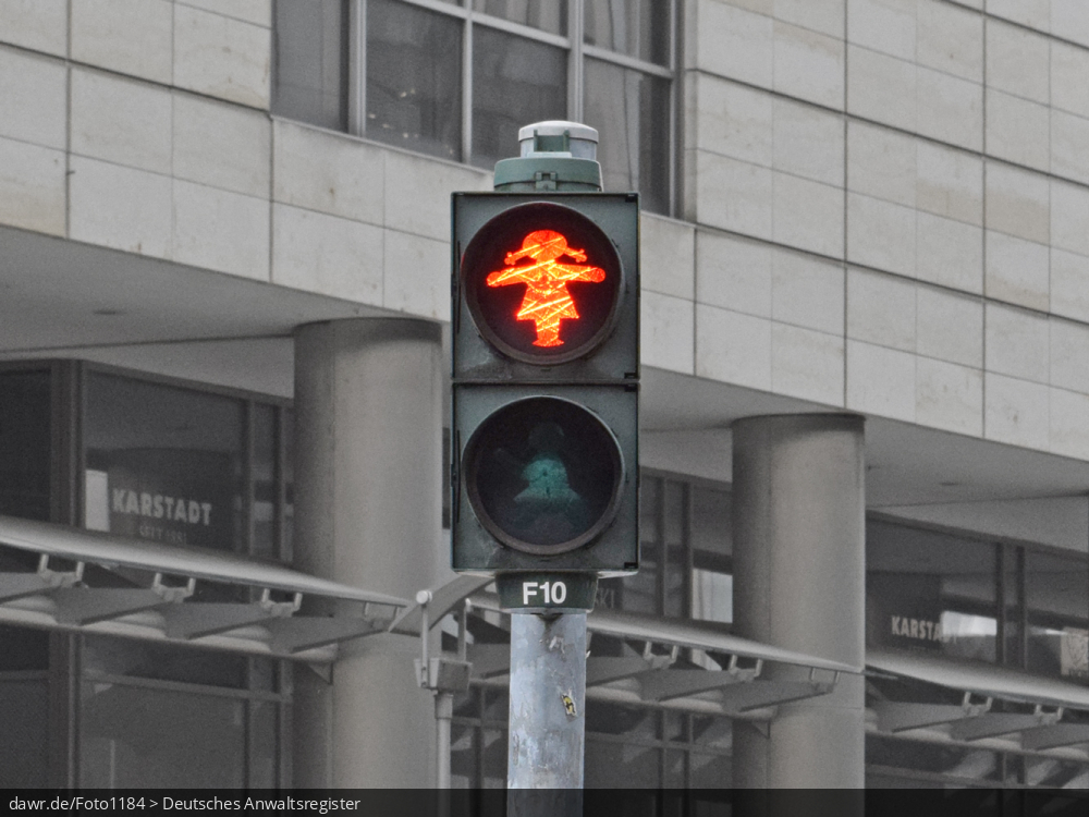 Dieses Foto zeigt eine rote Fußgängerampel, welche die Ampelfrau (die weibliche Version des berühmten ostdeutschen Ampelmännchens) als Symbolik verwendet. Diese Darstellungsform wurde erst 1996 vom Graphiker Hans-Jürgen Ellenberger im Sinne der Geschlechtergerechtigkeit entworfen und wird allerdings nur von wenigen Städten bei Lichtsignalanlagen verwendet.