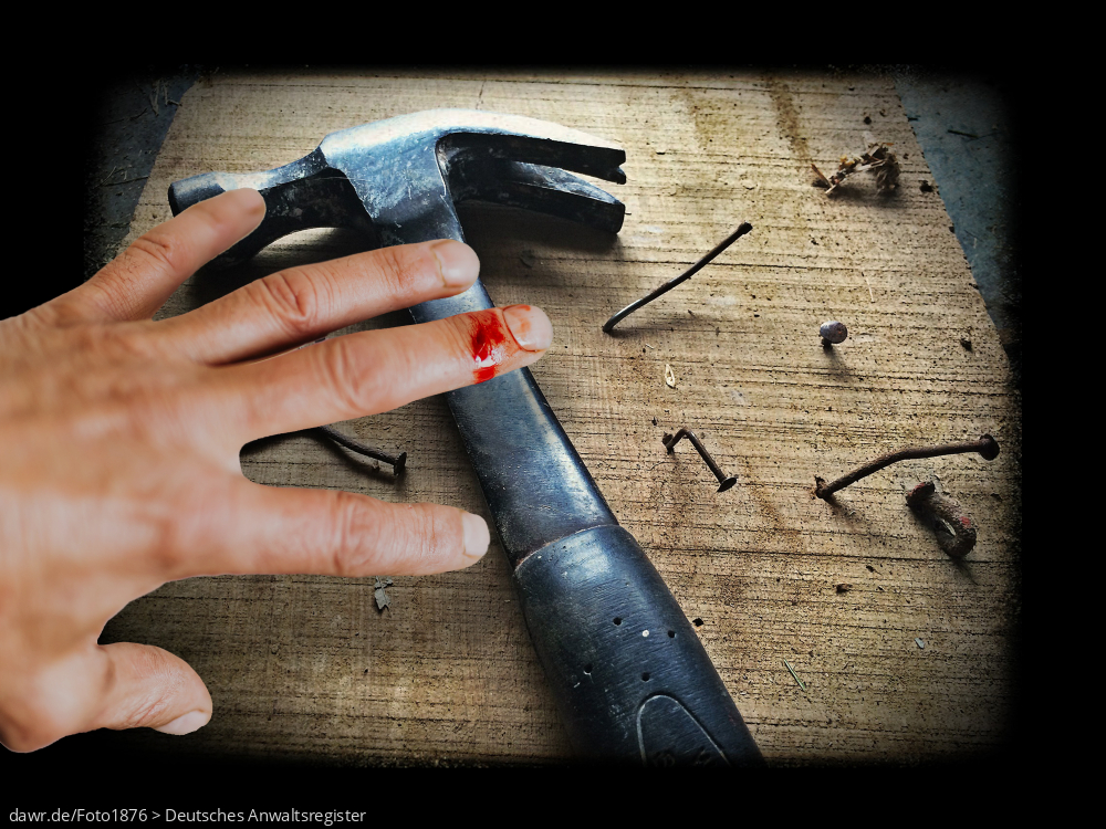 Dieses Bild zeigt eine Arbeitsfläche mit verschiedenen, krumm geschlagenen Nägeln und einem Hammer. Darüber ist eine Hand mit einem blutenden Finger zu sehen. Diese Darstellung eignet sich gut für Themen wie Arbeitsunfall und Sicherheit am Arbeitsplatz.