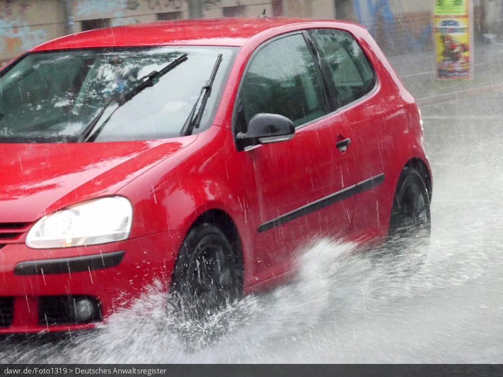 Dieses Foto zeigt einen Auto, wie während eines starken Regens durch eine Pfütze fährt. Dieses Bild ist gut als symbolische Darstellung für die Themen Unwetter und Starkregen geeignet.