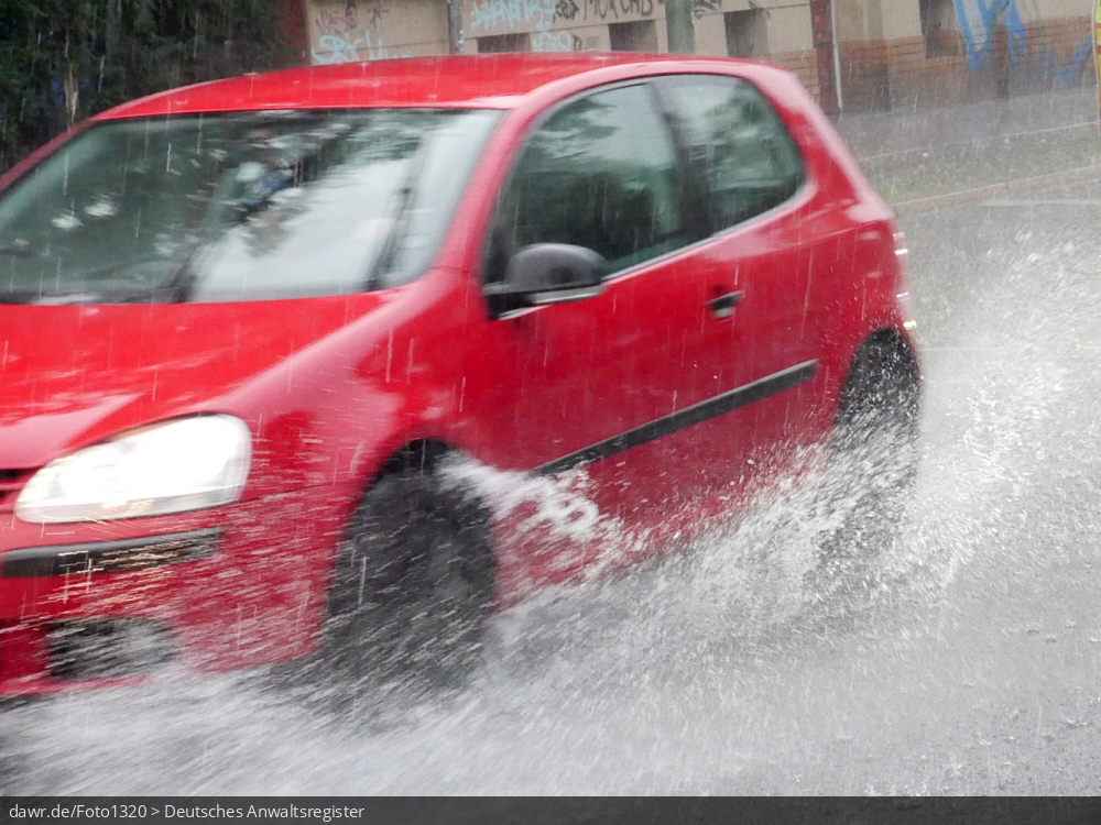 Dieses Foto zeigt einen Auto, wie während eines starken Regens durch eine Pfütze fährt. Dieses Bild ist gut als symbolische Darstellung für die Themen Unwetter und Starkregen geeignet.