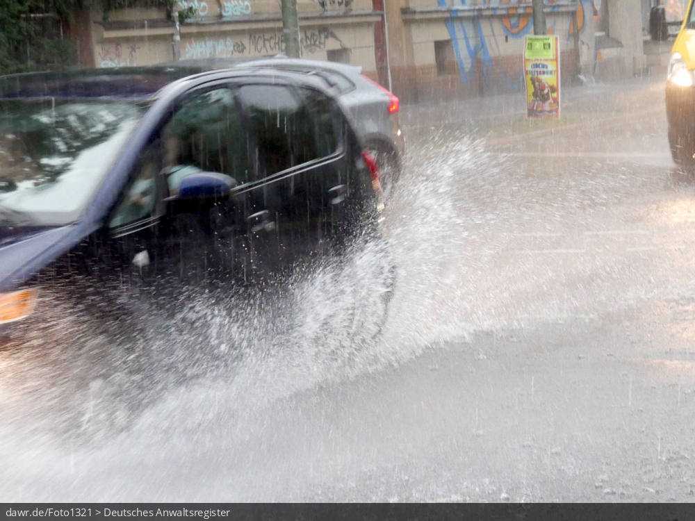 Dieses Foto zeigt einen Auto, wie während eines starken Regens durch eine Pfütze fährt. Dieses Bild ist gut als symbolische Darstellung für die Themen Unwetter und Starkregen geeignet.