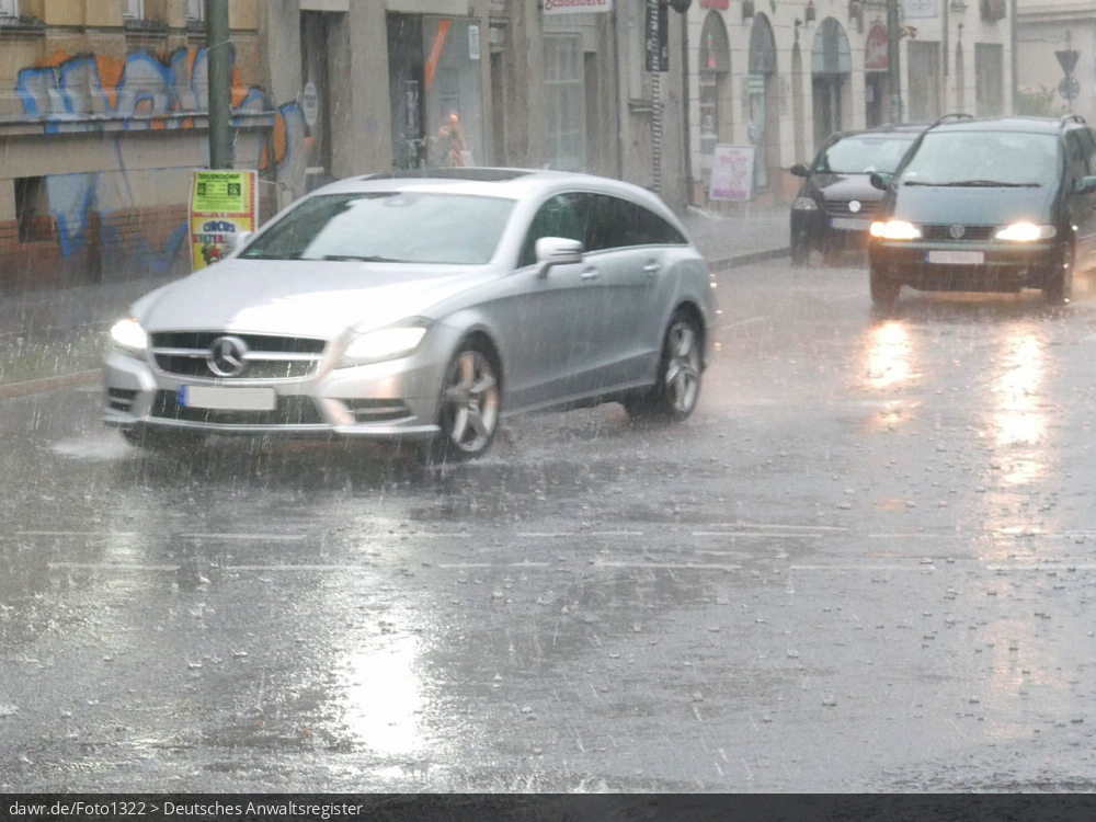Dieses Foto zeigt einen Auto, wie während eines starken Regens durch eine Pfütze fährt. Dieses Bild ist gut als symbolische Darstellung für die Themen Unwetter und Starkregen geeignet.