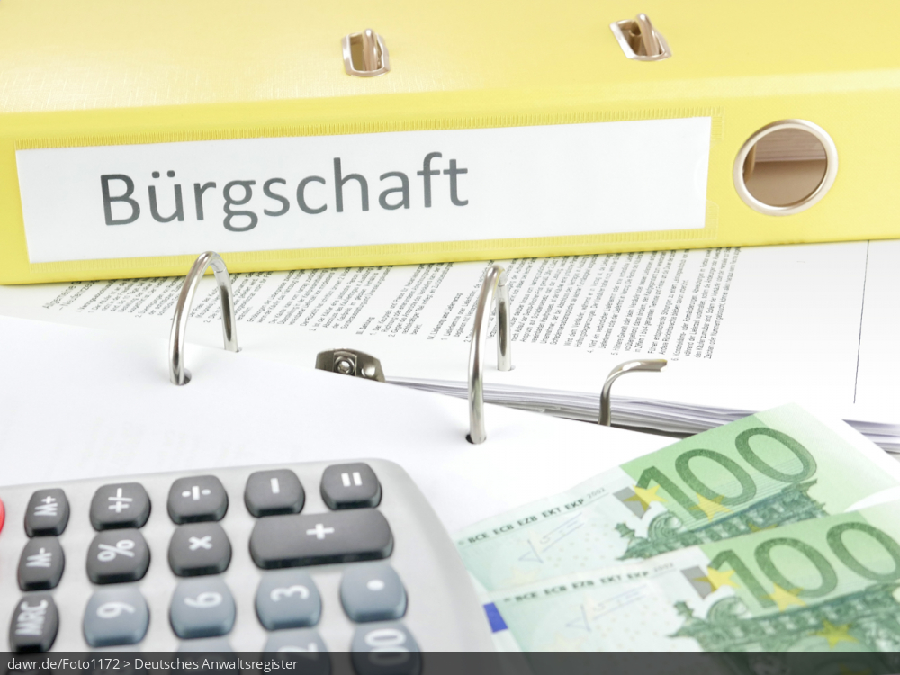 Dieses Foto zeigt einen gelben Aktenordner, mit der Beschriftung &bdquo;Bürgschaft&ldquo;, wobei der Ordner auf einem aufgeschlagenen und mit Dokumenten gefüllten Aktenordner liegt. Ebenfalls auf diesem aufgeschlagenen Ordner ist ein Tischrechner und mehrere Geldscheine zu finden. Dieses Bild eignet sich gut als symbolische Darstellung des Themas &bdquo;Bürgschaft und ihre Konsequenzen&ldquo;.