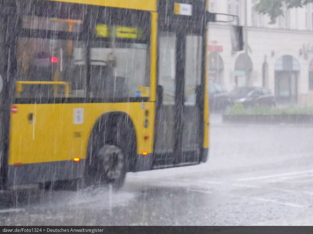 Dieses Foto zeigt einen Linienbus, wie während eines starken Regens durch eine Pfütze fährt. Dieses Bild ist gut als symbolische Darstellung für die Themen Unwetter und Starkregen geeignet.