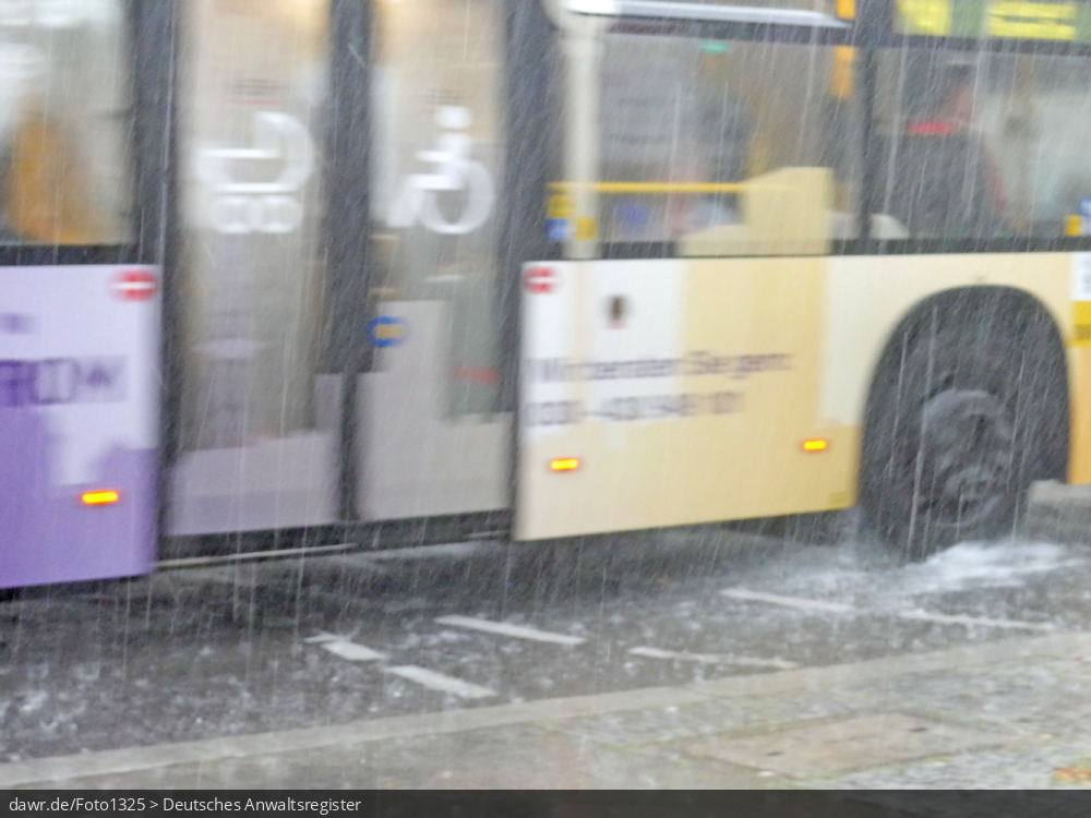 Dieses Foto zeigt einen Linienbus, wie während eines starken Regens durch eine Pfütze fährt. Dieses Bild ist gut als symbolische Darstellung für die Themen Unwetter und Starkregen geeignet.