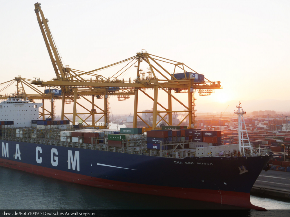 Dieses Foto zeigt einen Teil eines halbvoll beladenes Containerschiff im Hafen von Barcelona (Spanien). Über dem Schiff sind zwei große Verladekräne zu sehen. Auf der Seitenwand des Containerschiff findet sich die Aufschrift CMA CGM als Hinweis auf die Reederei.