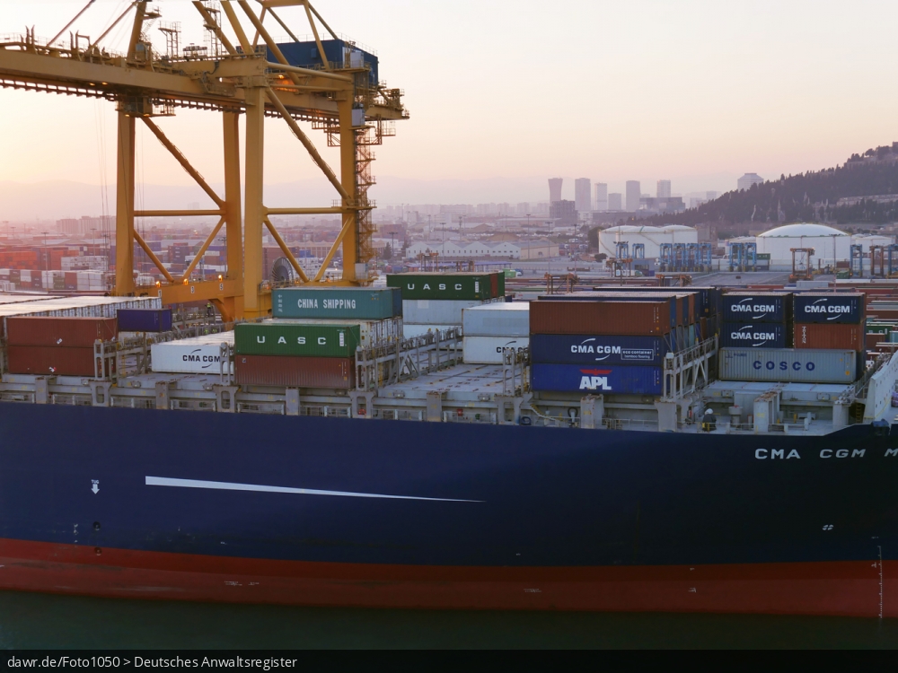 Dieses Foto zeigt einen Teil eines halbvoll beladenes Containerschiff im Hafen von Barcelona (Spanien). Über dem Schiff ist ein großer Verladekran zu sehen.