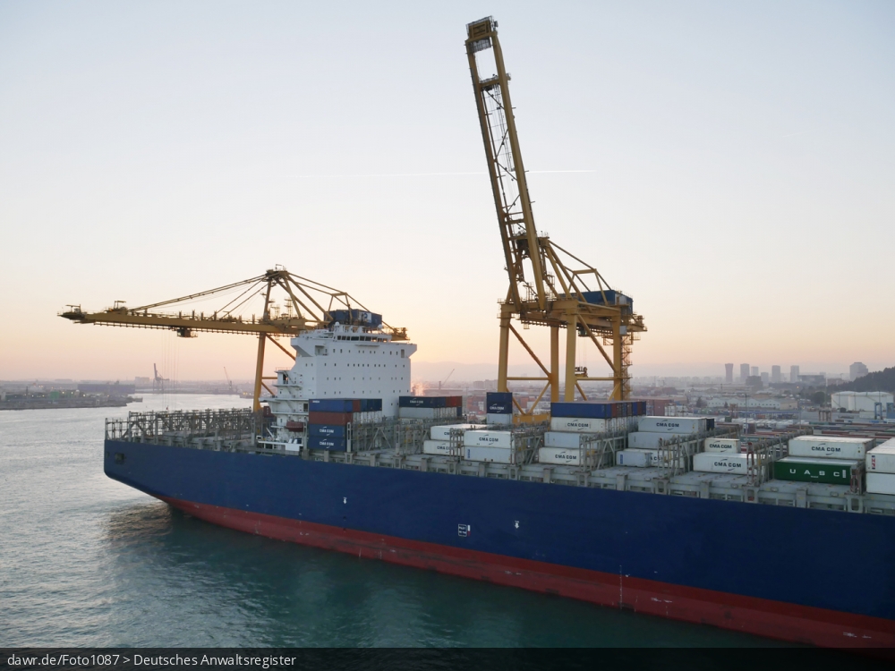 Dieses Foto zeigt einen Teil eines halbvoll beladenes Containerschiff im Hafen von Barcelona (Spanien). Im Hintergrund sind zwei große Verladekräne zu sehen.