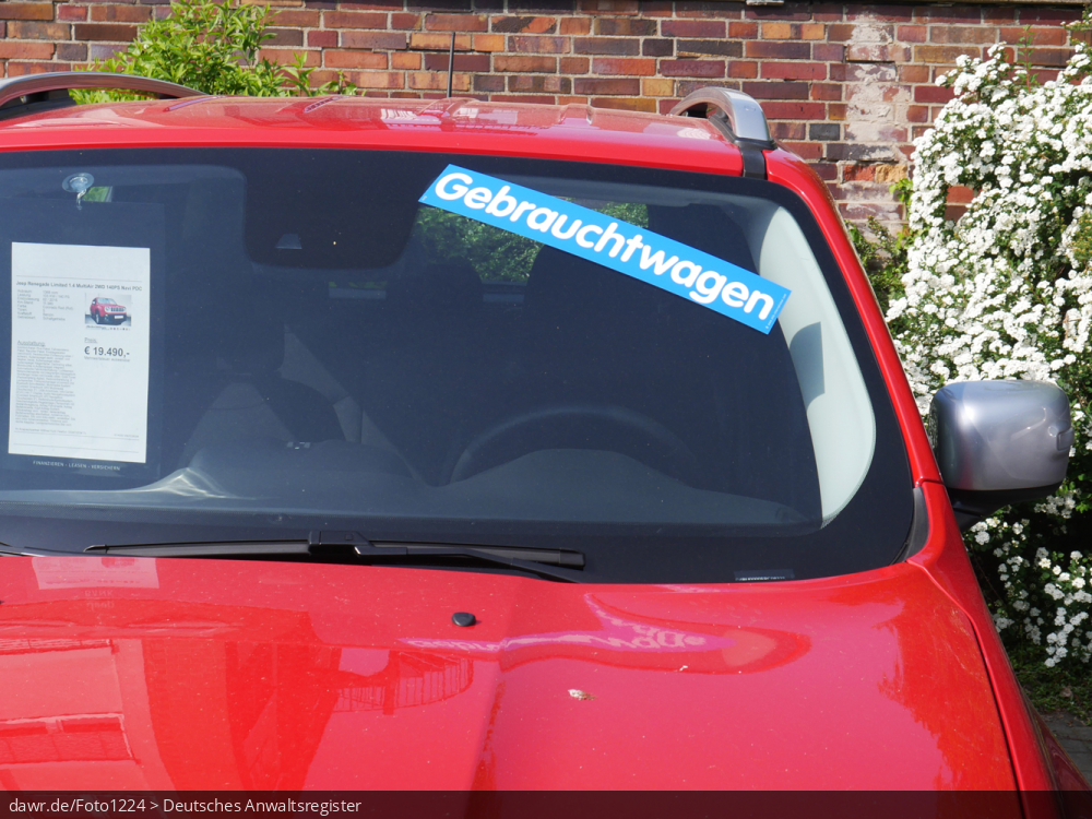 Dieses Foto zeigt Teile von der Front eines Autos, welches offenbar von einem Gebrauchtwagenhändler zum Kauf angeboten wird. Auf der Windschutzscheibe befindet sich ein Aufkleber mit dem Wort „Gebrauchtwagen“. Hinter der Scheibe sieht man ein Exposé zu diesem Fahrzeug, wie es Gebrauchtwagenhändler typischerweise für Ihre Fahrzeuge erstellen. Dieses Bild eignet sich gut als symbolische Darstellung für alle Rechtsstreitigkeiten in Zusammenhang mit Gebrauchtwagen.
