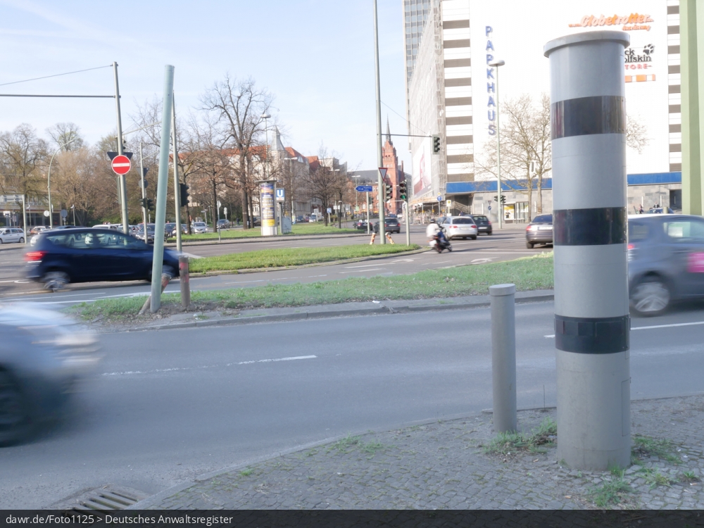 Dieses Foto zeigt eine große Straßenkreuzung, an der eine Geschwindigkeitsüberwachungsanlage vom Typ Vitronic Poliscan speed aufgestellt wurde. Auch wenn hier ein spezieller Typ von Geschwindigkeitsüberwachungsanlage dargestellt wird, ist es möglich dieses Bild als symbolische Darstellung für Themen in Zusammenhang mit Geschwindigkeitsverstößen und ihren Konsequenzen zu verwenden.