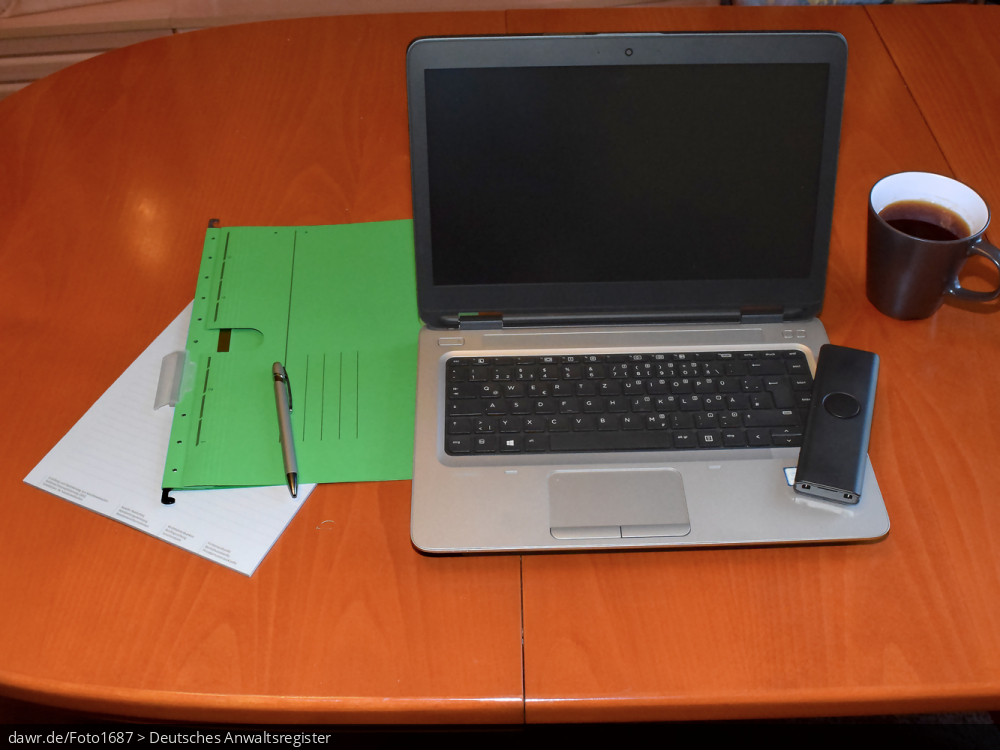 Dieses Foto zeigt einen Holztisch auf dem ein Notebook, ein Telefon, ein Block und ein Hängehefter zu sehen sind. Ergänzt wird die Szenerie durch einen Kugelschreiber und eine Kaffeetasse (oder Teetasse). Dieses Bild eignet sich gut als symbolische Darstellung für das Thema Home-Office, wie es im Zusammenhang mit der Corona-Pandemie sehr populär geworden ist.