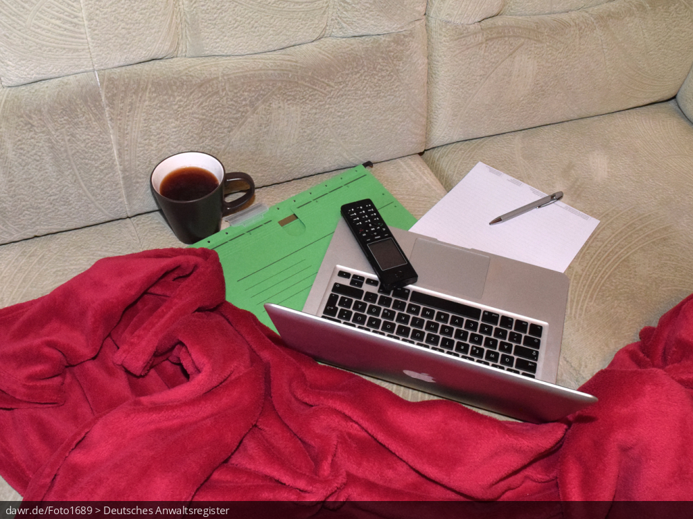 Dieses Foto zeigt ein Sofa auf dem ein Notebook, ein Telefon, ein Block (mit Kugelschreiber) und ein Hängehefter zu sehen sind. Umrahmt wird die Szenerie durch eine rote Decke, wie sie viele auf ihrer Couch liegen haben. Zusätzlich dazu ist noch eine Kaffeetasse (oder Teetasse) abgebildet Dieses Bild eignet sich gut als symbolische Darstellung für das Thema Home-Office, wie es im Zusammenhang mit der Corona-Pandemie sehr populär geworden ist.