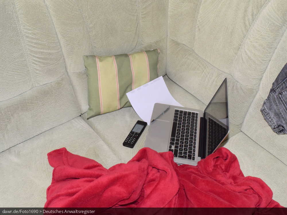 Dieses Foto zeigt ein Sofa auf dem ein Notebook, ein Telefon, ein Block und ein Kugelschreiber liegen. Ergänzt wird die Szenerie durch ein Sofakissen und eine rote Decke, wie sie viele auf ihrer Couch liegen haben. Dieses Bild eignet sich gut als symbolische Darstellung für das Thema Home-Office, wie es im Zusammenhang mit der Corona-Pandemie sehr populär geworden ist.