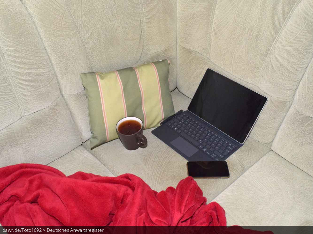 Dieses Foto zeigt ein Sofa auf dem ein Tablet (mit Zusatztastatur), ein Smartphone und eine Kaffeetasse (oder Teetasse) stehen. Umrahmt wird die Szenerie durch ein Sofakissen und eine rote Decke, wie sie viele auf ihrer Couch liegen haben. Dieses Bild eignet sich gut als symbolische Darstellung für das Thema Home-Office, wie es im Zusammenhang mit der Corona-Pandemie sehr populär geworden ist.