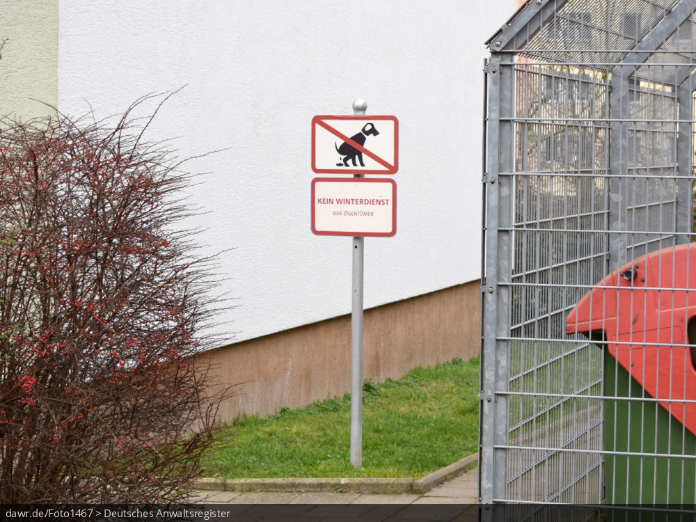 Dieses Foto zeigt zwei Hinweisschilder, die neben einem Müllhäuschen in einem Wohngebiet stehen. Neben dem Verbot von Hunden, wird darauf hingewiesen, dass hier kein Winterdienst durchgeführt wird. Diese Abbildung eignet sich gut als symbolische Darstellung für Themen, wie Hunde, Winterdienst, sowie Vermieter- bzw. Mieterrechte.