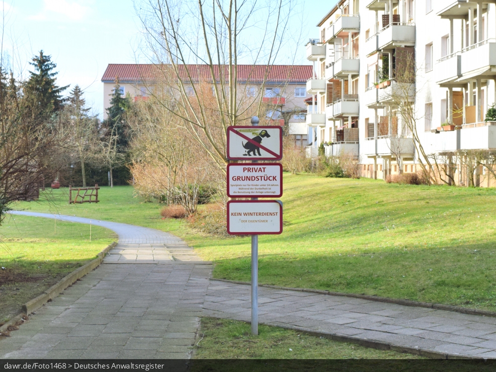 Dieses Foto zeigt den Innenhof einer Wohnsiedlung mit drei Hinweisschildern. Neben dem Verbot von Hunden und Hinweisen bez. des (im Hintergrund erahnbaren) Spielplatzes, wird darauf hingewiesen, dass hier kein Winterdienst durchgeführt wird. Diese Abbildung eignet sich gut als symbolische Darstellung für Themen, wie Hunde, Spielplatz, Winterdienst, sowie Vermieter- bzw. Mieterrechte.