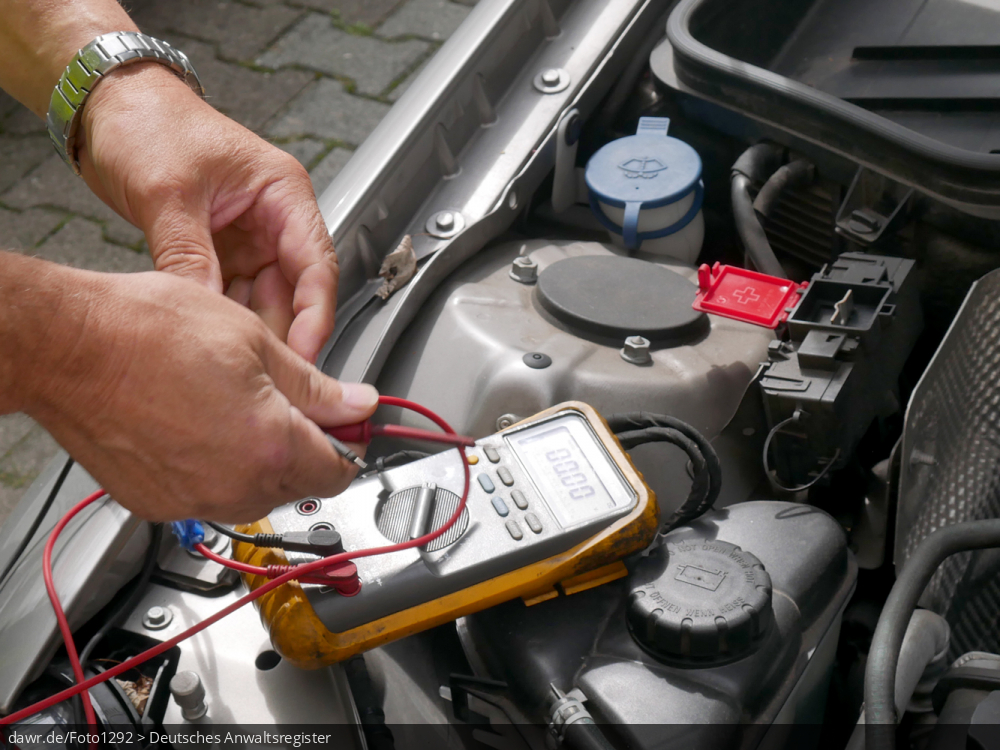 Dieses Foto zeigt den Motorraum eines PKW, in dem ein Strommessgerät liegt, mit dem ein Automechaniker die Batterie prüft. Diese Darstellung eignet sich gut als Symbolik für alle Themen rund ums Auto und die Autoreparatur.