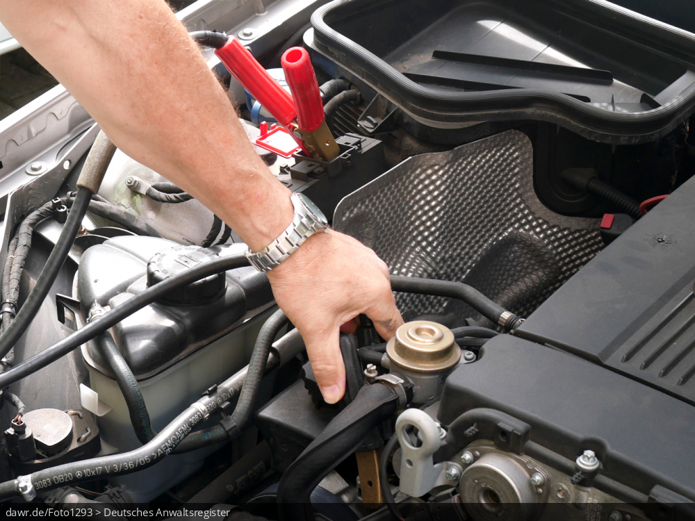 Dieses Foto zeigt den Motorraum eines PKW, in dem ein Automechaniker mit seiner Hand die Kontakte der Batterie prüft. Diese Darstellung eignet sich gut als Symbolik für alle Themen rund ums Auto und die Autoreparatur.