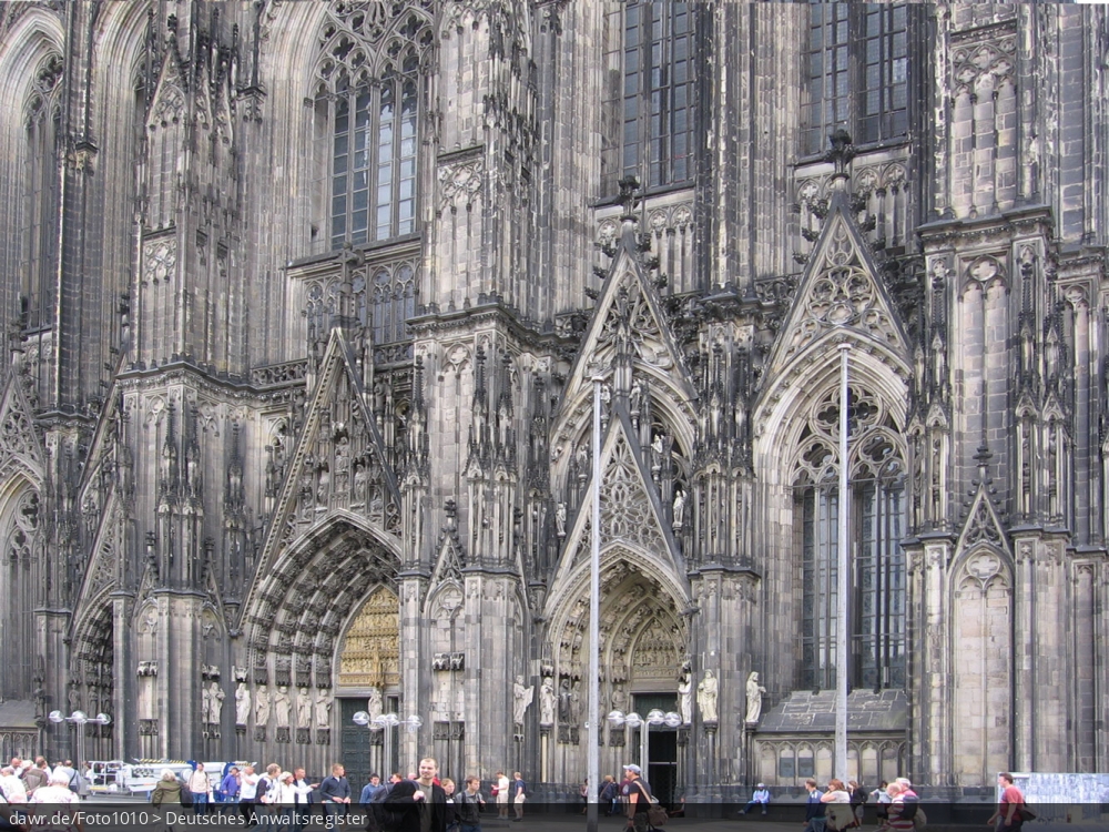 Dieses Foto zeigt der Kölner Dom, ein zum UNESCO-Weltkulturerbe gehörende Kathedrale des Erzbistums Köln und Wahrzeichen der Stadt Köln. Es wird der Eingangsbereich mit verschiedenen Passanten gezeigt.