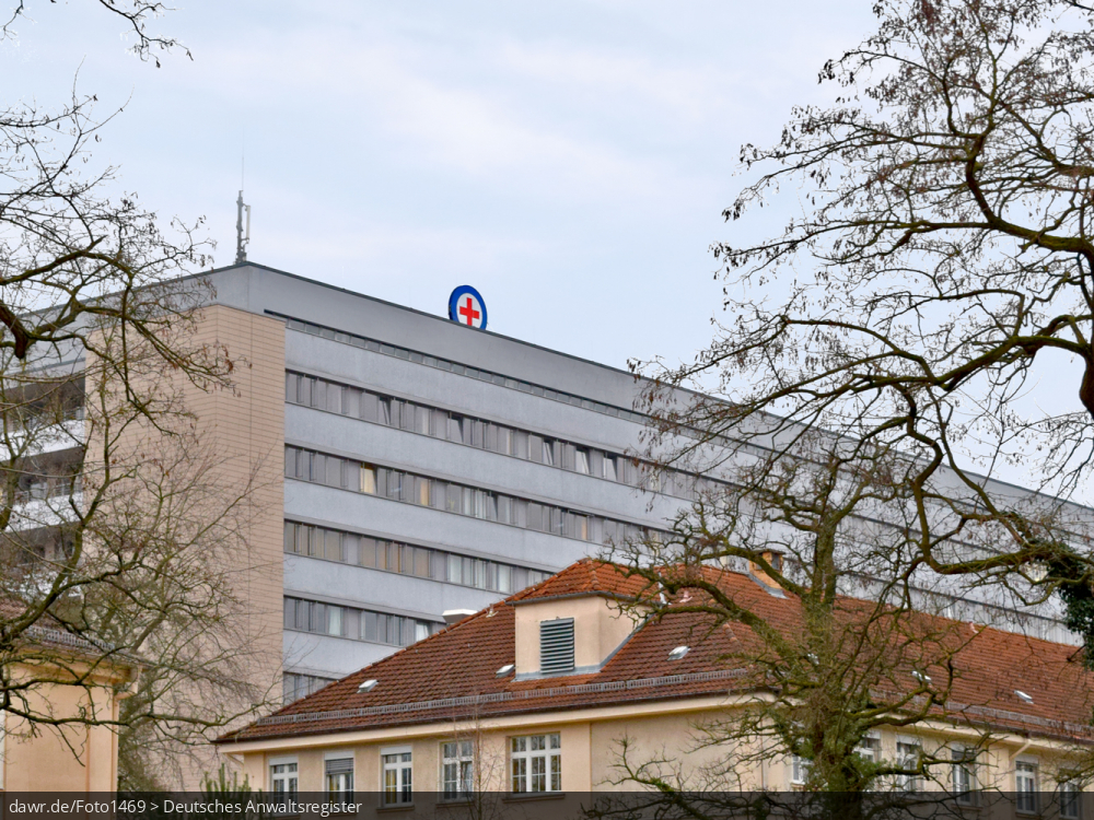 Dieses Foto zeigt das Bettenhaus eines großen Krankenhauses mit dem Roten Kreuz auf dem Dach. Diese Abbildung eignet sich gut als symbolische Darstellung für die Themen Krankenhaus und Gesundheit.