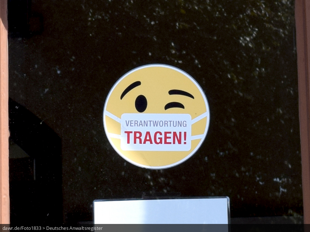 Dieses Foto zeigt einen Aufkleber auf einer Eingangstür, der einen Smilie mit einem Mundschutz zeigt und so zum Einhalten der allgemeinen Maskenpflicht auffordert. Diese symbolische Darstellung eignet sich gut für alle Themen im Zusammenhang mit einer staatlich angeordneten Maskenpflicht bspw. im Rahmen der Corona-Pandemie.