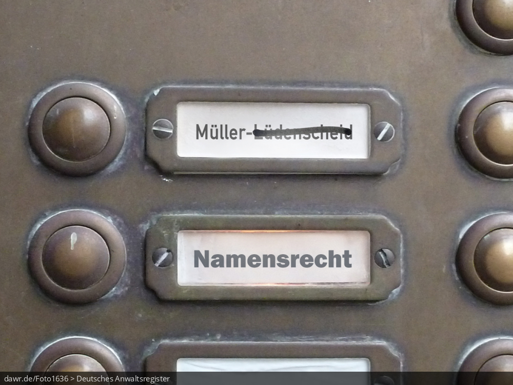 Dieses Foto zeigt einen Teil des Klingelschilds eines Altbau-Mehrfamilienhauses, wobei die Namen „Müller-Lüdenscheid“ und „Namensrecht“ zu lesen sind. Der Zusatz „Lüdenscheid“ wurde durchgestrichen, wie es bspw. nach einer Scheidung nötig sein könnte. Diese symbolische Darstellung eignet sich gut für alle Themen rund um das Namensrecht, speziell bez. des Umgangs mit dem Familiennamen bei einer Scheidung.