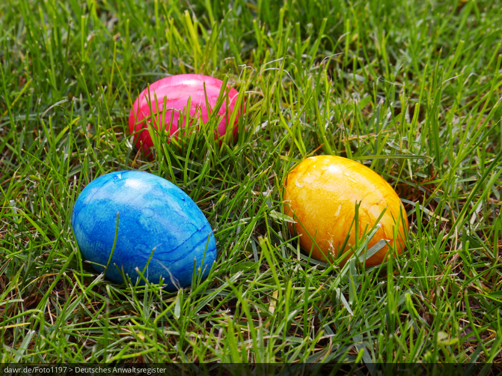 Dieses Foto zeigt drei bunte Ostereier, die im Gras liegen. Eine solches Bild eignet sich gut als symbolische Darstellung für das Osterfest.