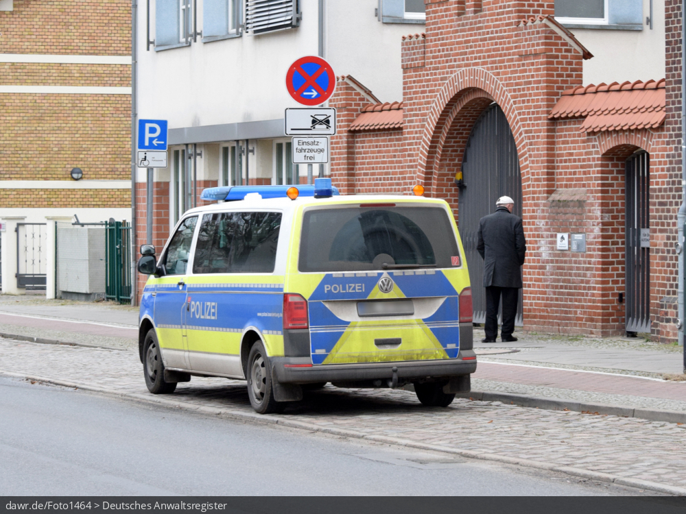 Dieses Foto zeigt einen Kleinbus der Polizei mit auffälliger Beklebung in Signalfarben. Das Fahrzeug steht auf einem speziell reservierten Parkplatz für Einsatzfahrzeuge, wie sie oft vor Polizeirevieren zu finden sind. Diese Abbildung eignet sich gut als symbolische Darstellung für die Themen Polizei und Verkehrsunfall.
