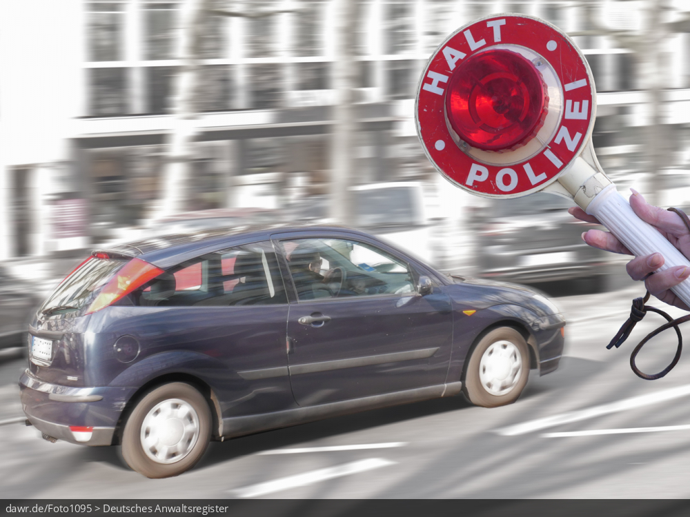 Dieses Foto zeigt im Hintergrund eine Straße mit einem zügig vorbeifahrendem Auto. Im Vordergrund sieht man einen Anhaltestab (gern als Polizeikelle bezeichnet) mit den Aufschriften „Halt“ und „Polizei“, wie er von Polizisten bei Fahrzeugkontrollen eingesetzt wird. Dieses Bild eignet sich gut als Symbolisierung von Fahrzeugkontrollen oder anderen Verkehrskontrollen durch die Polizei.