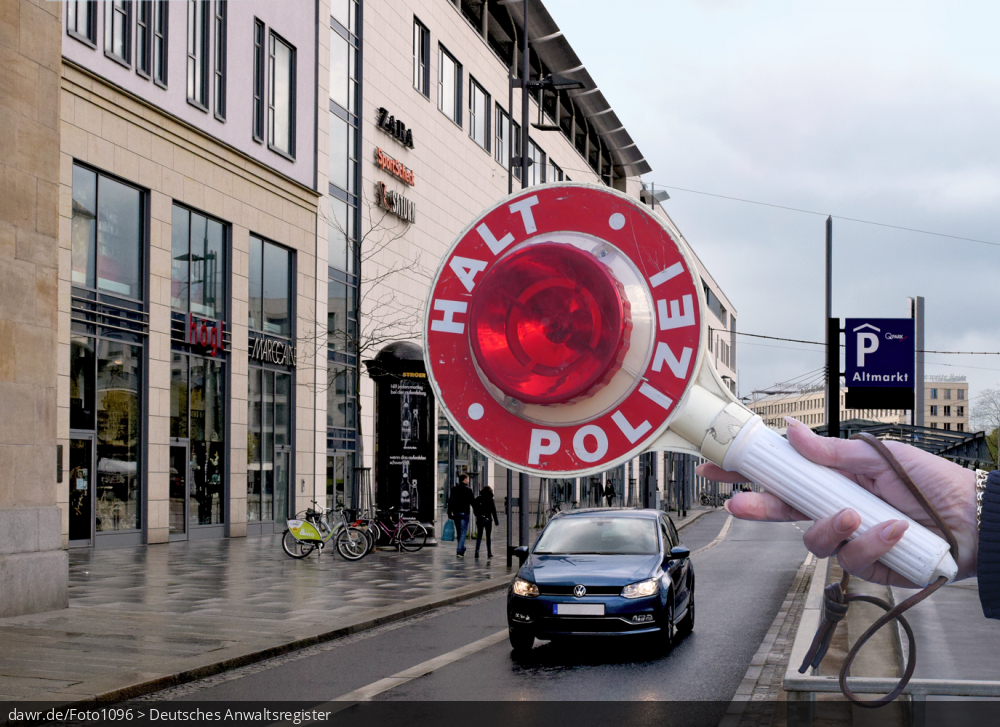 Dieses Foto zeigt im Hintergrund eine Straße in einer Großstadt mit einem zügig heranfahrendem Auto. Im Vordergrund sieht man einen Anhaltestab (gern als Polizeikelle bezeichnet) mit den Aufschriften „Halt“ und „Polizei“, wie er von Polizisten bei Fahrzeugkontrollen eingesetzt wird. Dieses Bild eignet sich gut als Symbolisierung von Fahrzeugkontrollen oder anderen Verkehrskontrollen durch die Polizei.