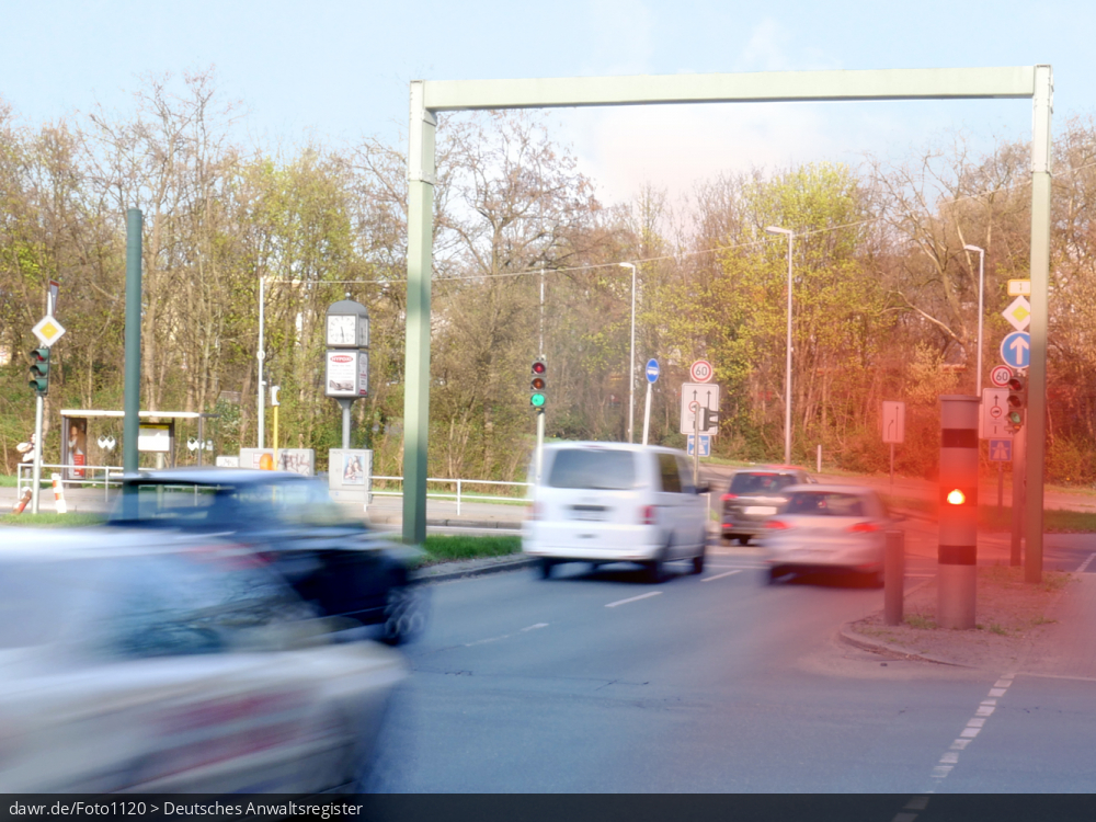 Dieses Foto zeigt eine große Straßenkreuzung, an der eine Geschwindigkeitsüberwachungsanlage vom Typ Vitronic Poliscan speed aufgestellt wurde, welche gerade ein Auto blitzt. Auch wenn hier ein spezieller Typ von Geschwindigkeitsüberwachungsanlage dargestellt wird, ist es möglich dieses Bild als symbolische Darstellung für Themen in Zusammenhang mit Geschwindigkeitsverstößen und ihren Konsequenzen zu verwenden.