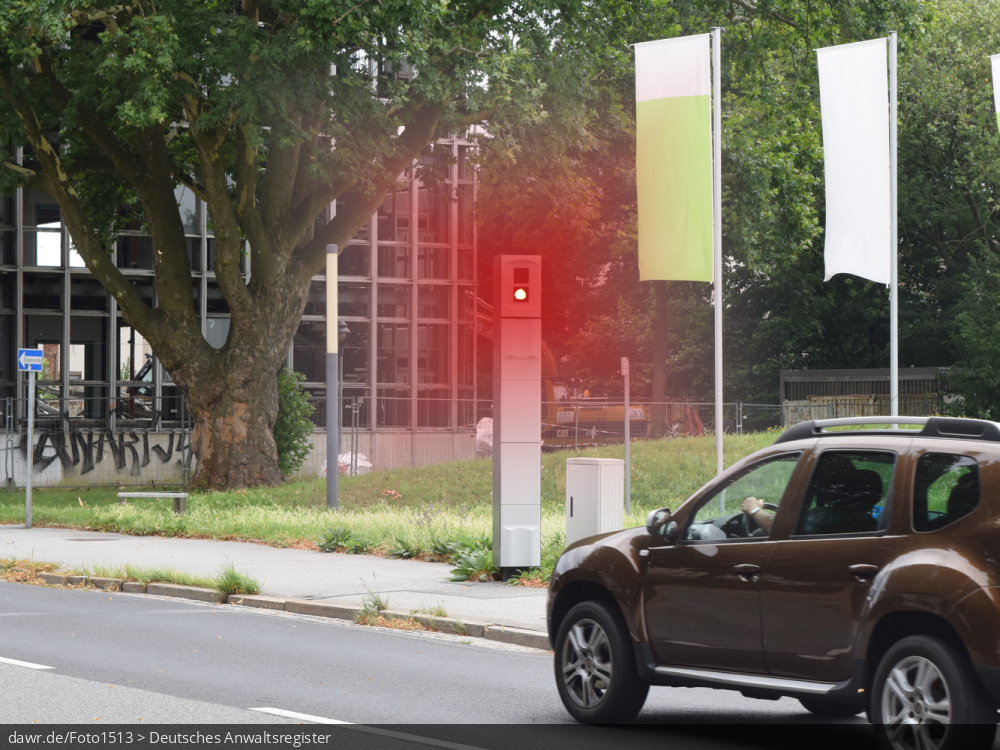 Dieses Foto zeigt eine stationäre Säule zur Geschwindigkeitskontrolle an einer Hauptstraße, welches gerade auslöst, um ein davor befindliches Auto zu fotografieren. Das Bild kann gut als symbolische Darstellung für Themen in Zusammenhang mit Geschwindigkeitsverstößen und ihren Konsequenzen verwendet werden.