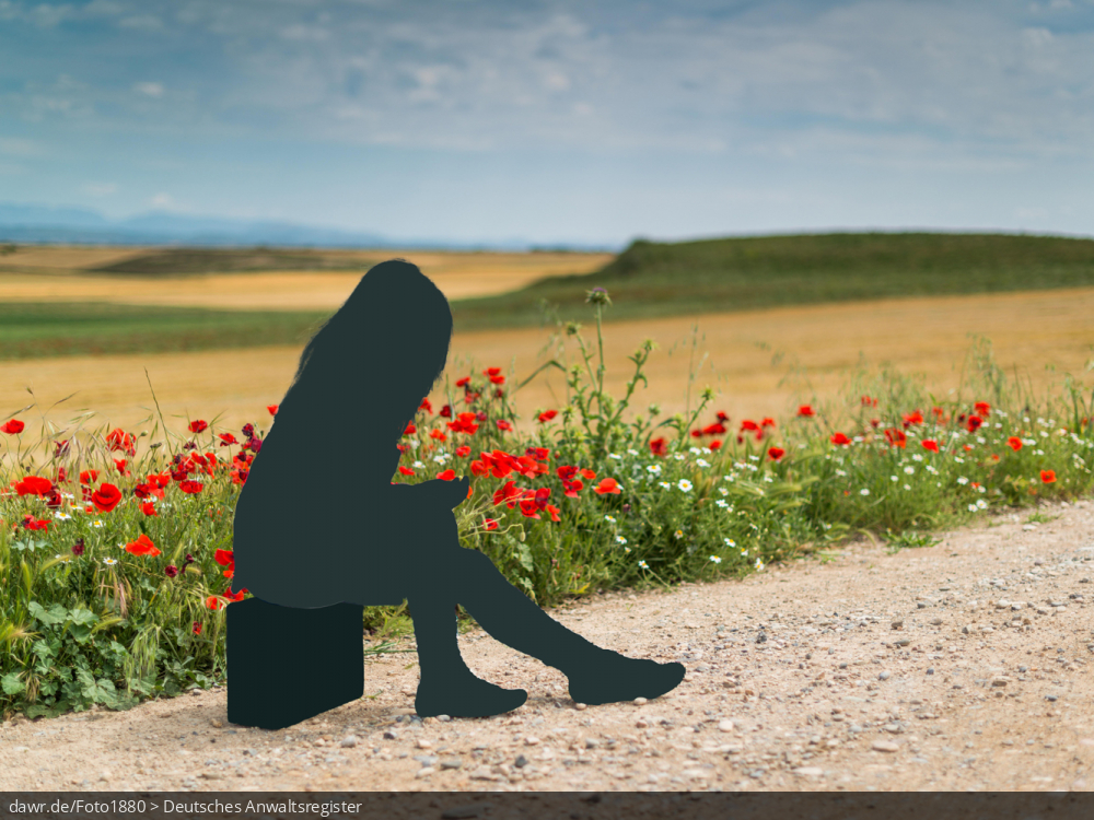 Dieses Foto zeigt eine offene Landschaft mit Wiesen, Feldblumen und einem Schotterweg. Auf diesem sitzt eine Faru auf ihrem Koffer. Die Frau und der Koffer sind allerdings nur als Silhouetten dargestellt, ganz so als wäre sie ausradiert worden. Diese Darstellung eignet sich wegen dem Ausradieren gut für das Thema Reiserücktritt.
