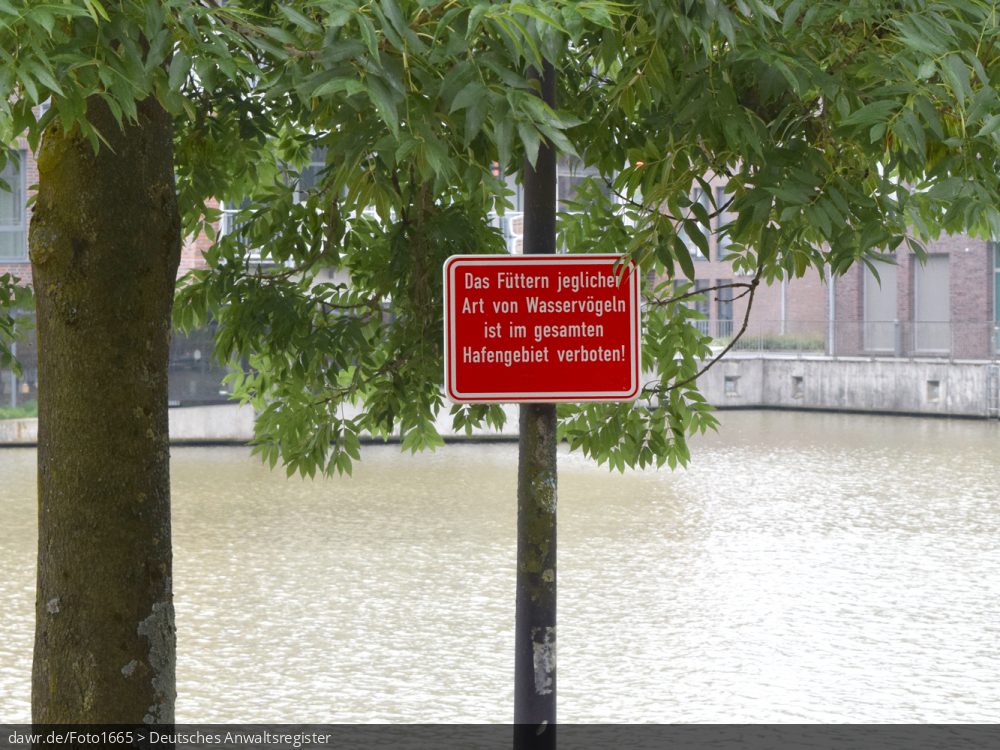 Dieses Foto zeigt ein Schild, welches das Füttern von Wasservögeln (bspq. Enten) verbietet, wie es von vielen Gemeinden an Ufern von Flüssen und Seen aufstellen. Dieses Bild ist eine passende symbolische Darstellung für die rechtliche Frage, wo das Füttern von Enten usw. erlaubt ist.
