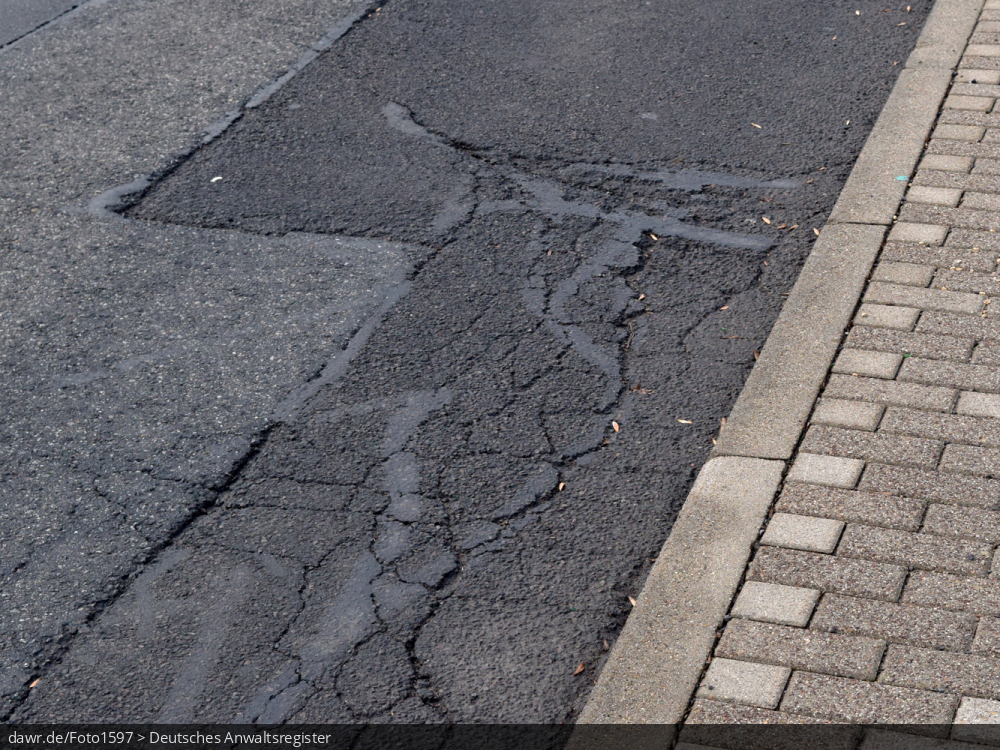 Dieses Foto zeigt eine Hauptverkehrsstraße in einer deutschen Stadt. Man sieht deutliche Risse im Asphalt und dies sogar auf bereits reparierten Straßenabschnitten. Dieses Bild ist gut als symbolhafte Darstellung für das Auftreten von Straßenschäden und die damit einhergehenden rechtlichen Fragen, bspw. im Schadenersatzrecht.