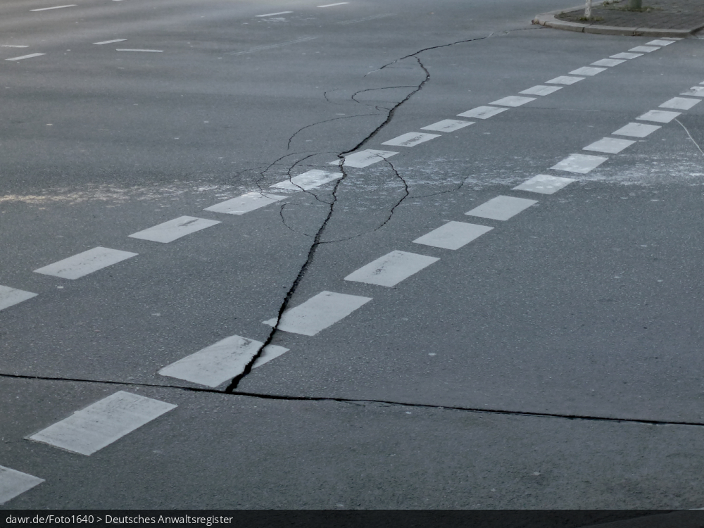 Dieses Foto zeigt eine Hauptverkehrsstraße in einer deutschen Stadt. Man sieht deutliche Risse im Asphalt. Dieses Bild ist gut als symbolhafte Darstellung für das Auftreten von Straßenschäden und die damit einhergehenden rechtlichen Fragen, bspw. im Schadenersatzrecht.