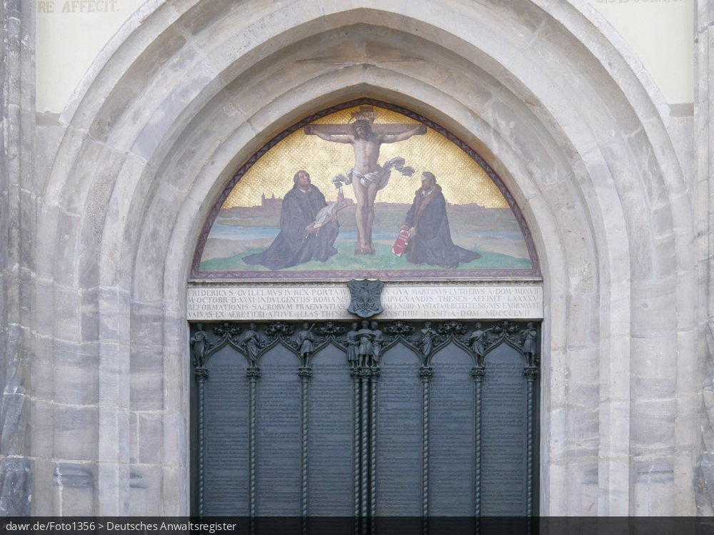 Dieses Foto zeigt den Tympanon am Thesenportal der Schlosskirche in der Lutherstadt Wittenberg, welche seit 1996 als UNESCO-Welterbestätte anerkannt ist. An diesem Portal schlug am 31. Oktober 1517 der Wittenberger Augustinermönch und Theologieprofessor Martin Luther seine 95 lateinischen Disputationsthesen zur Reform der Kirche an.
