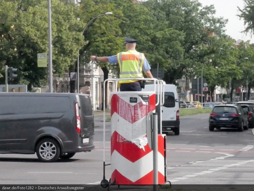 Dieses Foto zeigt einen Verkehrspolizisten, welche den Verkehr auf einer großen Straßenkreuzung regelt, womit es sich gut für das Thema Verkehr im Städten eignet.