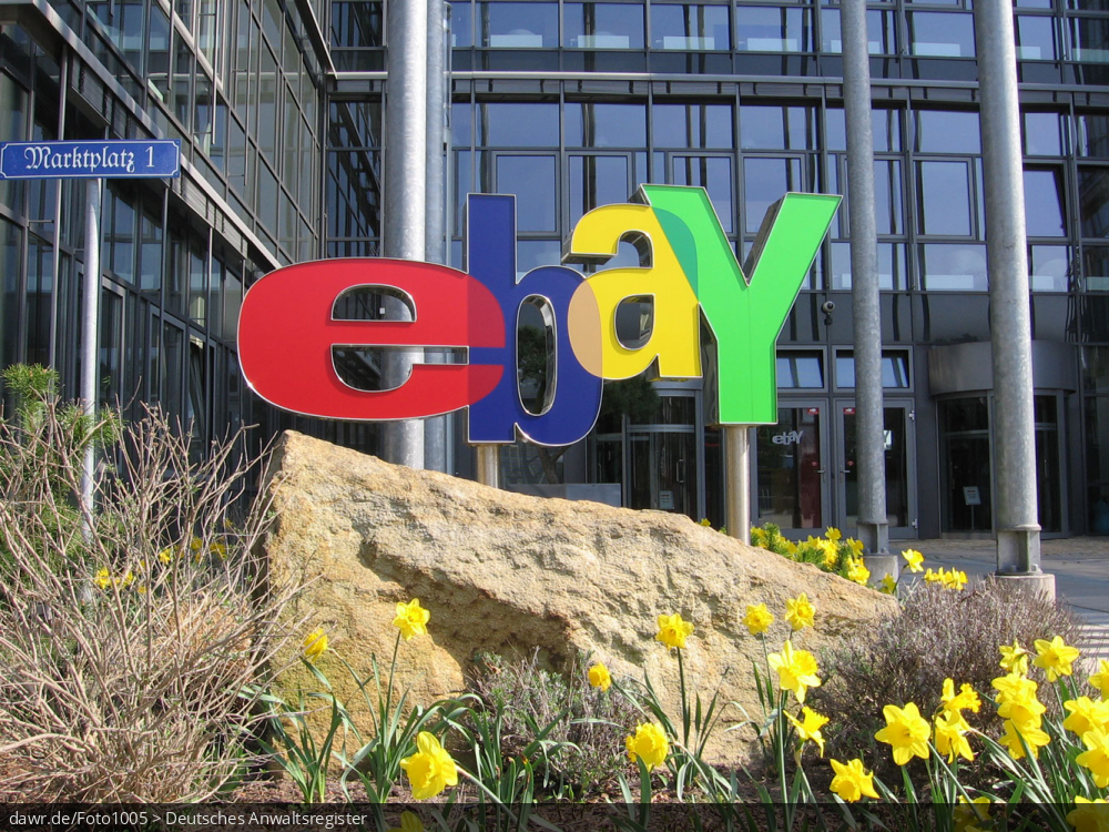 Dieses Foto zeigt das Logo von eBay. Im Hintergrund ist der Eingang der deutschen Niederlassung des großen Online-Auktionshauses im brandenburgischen Kleinmachnow zu sehen.