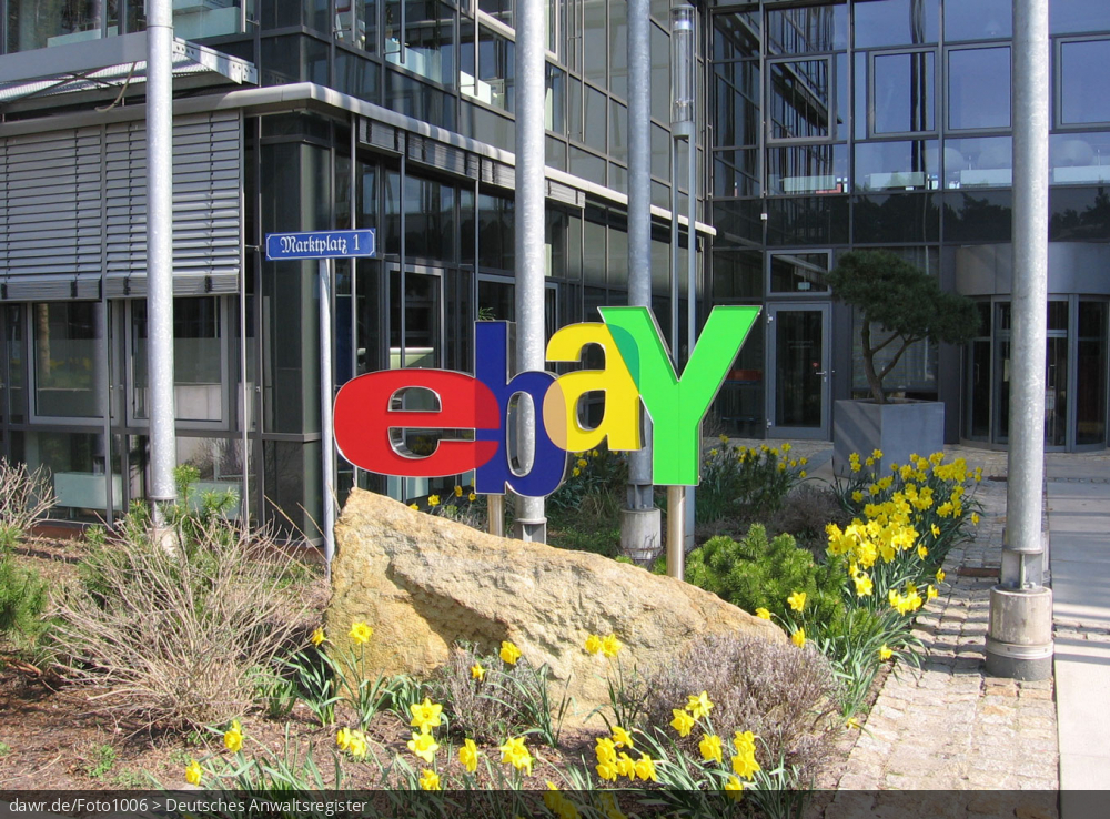 Dieses Foto zeigt das Logo von eBay. Im Hintergrund ist der Eingang der deutschen Niederlassung des großen Online-Auktionshauses im brandenburgischen Kleinmachnow zu sehen.