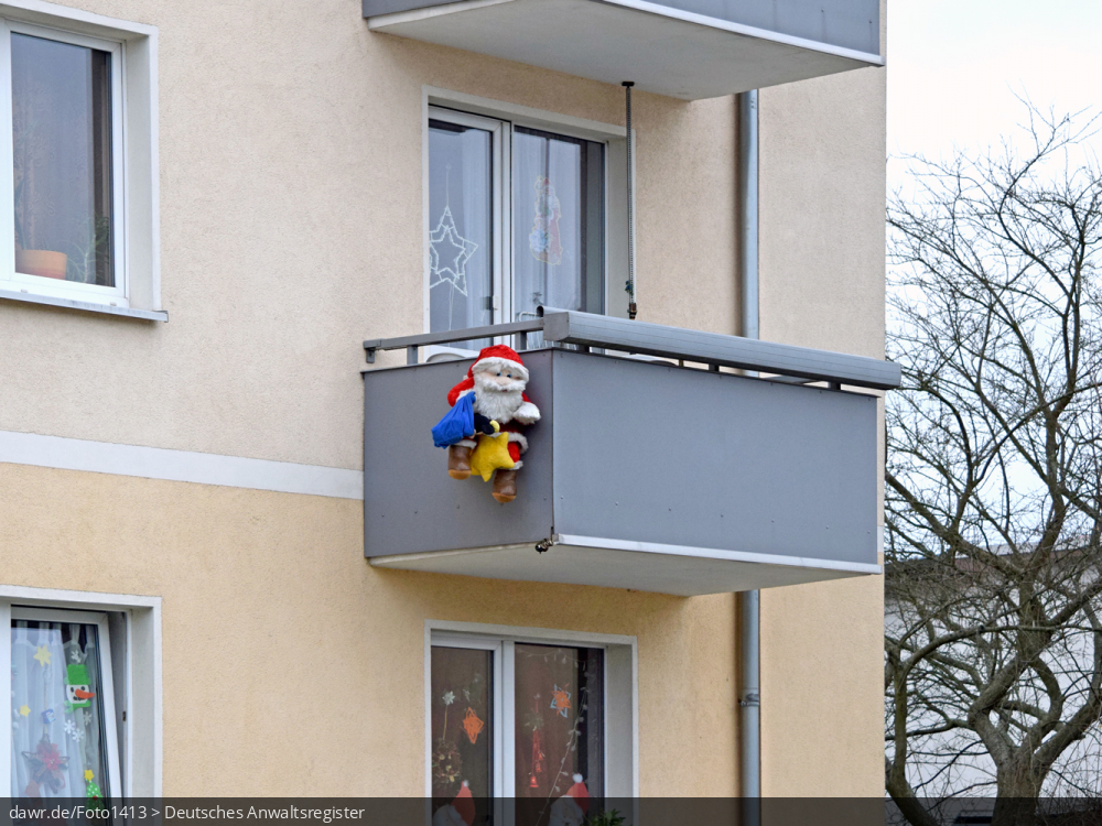 Dieses Foto zeigt einen Weihnachtsmann, welcher am Balkon eines Mehrfamilienhauses hängt. In der heutigen Zeit sind solche Figuren eine gern genutzte Weihnachtsdekoration. Dieses Bild eignet sich gut als symbolische Darstellung für alle Themen rund um Weihnachten und speziell zu rechtlichen Fragen bez. der Weihnachtsdekoration.