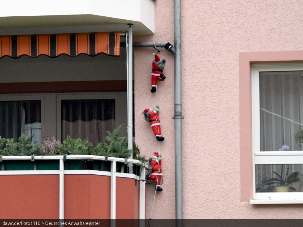 Dieses Foto zeigt drei Weihnachtsmänner, welche an einen Seil die Fassade eines Mehrfamilienhauses hochklettern. In der heutigen Zeit sind solche Figuren eine gern genutzte Weihnachtsdekoration. Dieses Bild eignet sich gut als symbolische Darstellung für alle Themen rund um Weihnachten und speziell zu rechtlichen Fragen bez. der Weihnachtsdekoration.