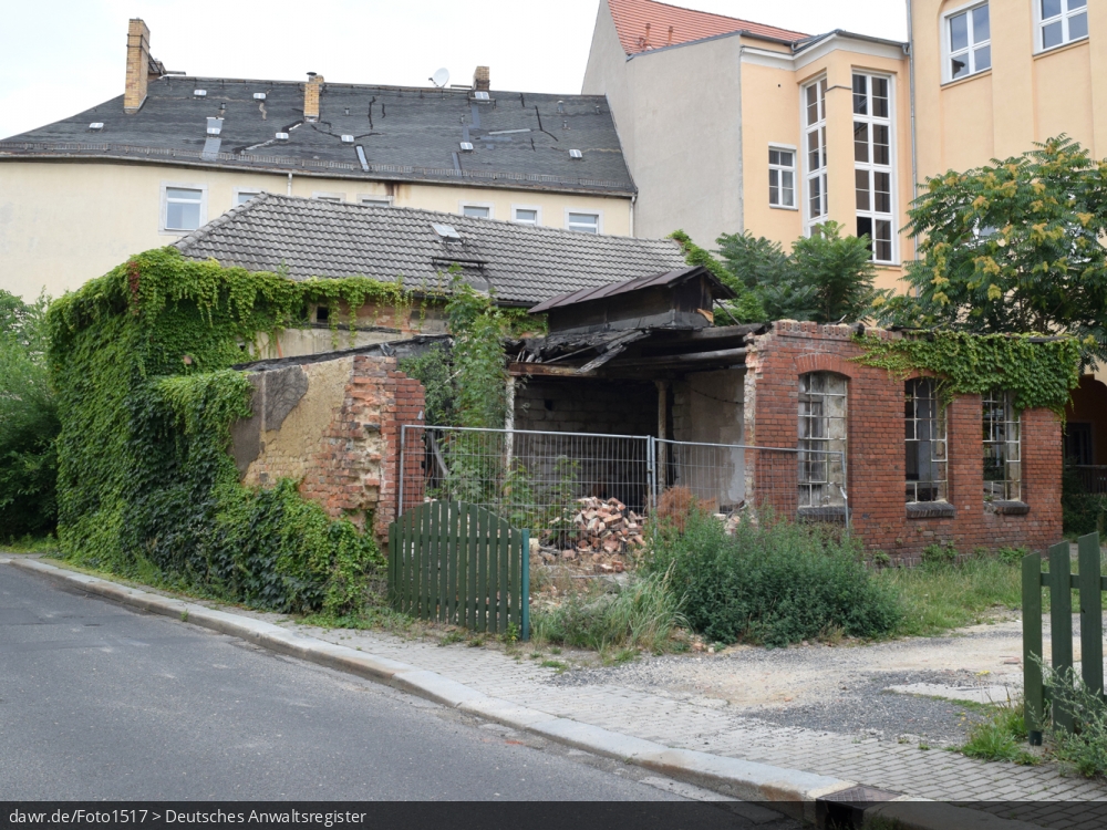 Dieses Foto zeigt eine baufälliges Haus mit teilweise eingestürztem Dach und eingefallenen Wänden, wie es in vielen (Klein)Städten zu finden ist. Die Gründe für einen solch schlechten Erhaltungszustand sind oft ungeklärte Eigentumsverhältnisse, ausbleibende staatliche Mittel oder einfach fehlende Investoren. Mit seinem schlechten Erhaltungszustand, kann dieses Gebäude symbolisch für Themen wie Wohnungsbau, Mietmängel oder auch Schrottimmobilien stehen.