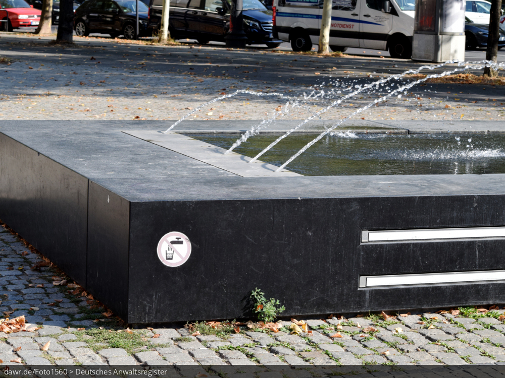 Dieses Foto zeigt einen Springbrunnen in einer Großstadt, an den ein Aufkleber zu finden ist, dass das Wasser im Brunnen nicht trinkbar ist.  Dieses Bild ist gut als symbolische Darstellung für Themen im Zusammenhang mit Trinkwasser geeignet.