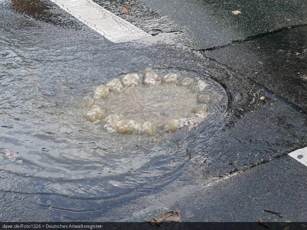 Dieses Foto zeigt eine wegen einem übergelaufenen Gulli überschwemmte Straße, als Folge eines Starkregens. Dieses Bild ist gut als symbolische Darstellung für die Themen Unwetter und Starkregen geeignet.