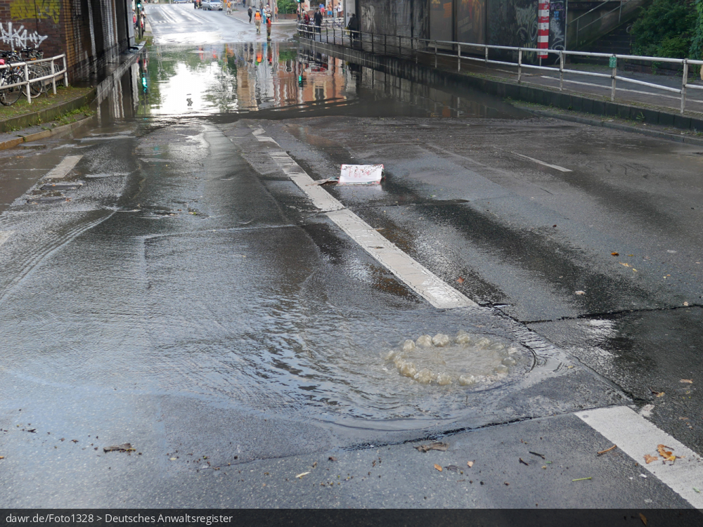 Dieses Foto zeigt eine wegen einem übergelaufenen Gulli überschwemmte Straße, als Folge eines Starkregens. Dieses Bild ist gut als symbolische Darstellung für die Themen Unwetter und Starkregen geeignet.